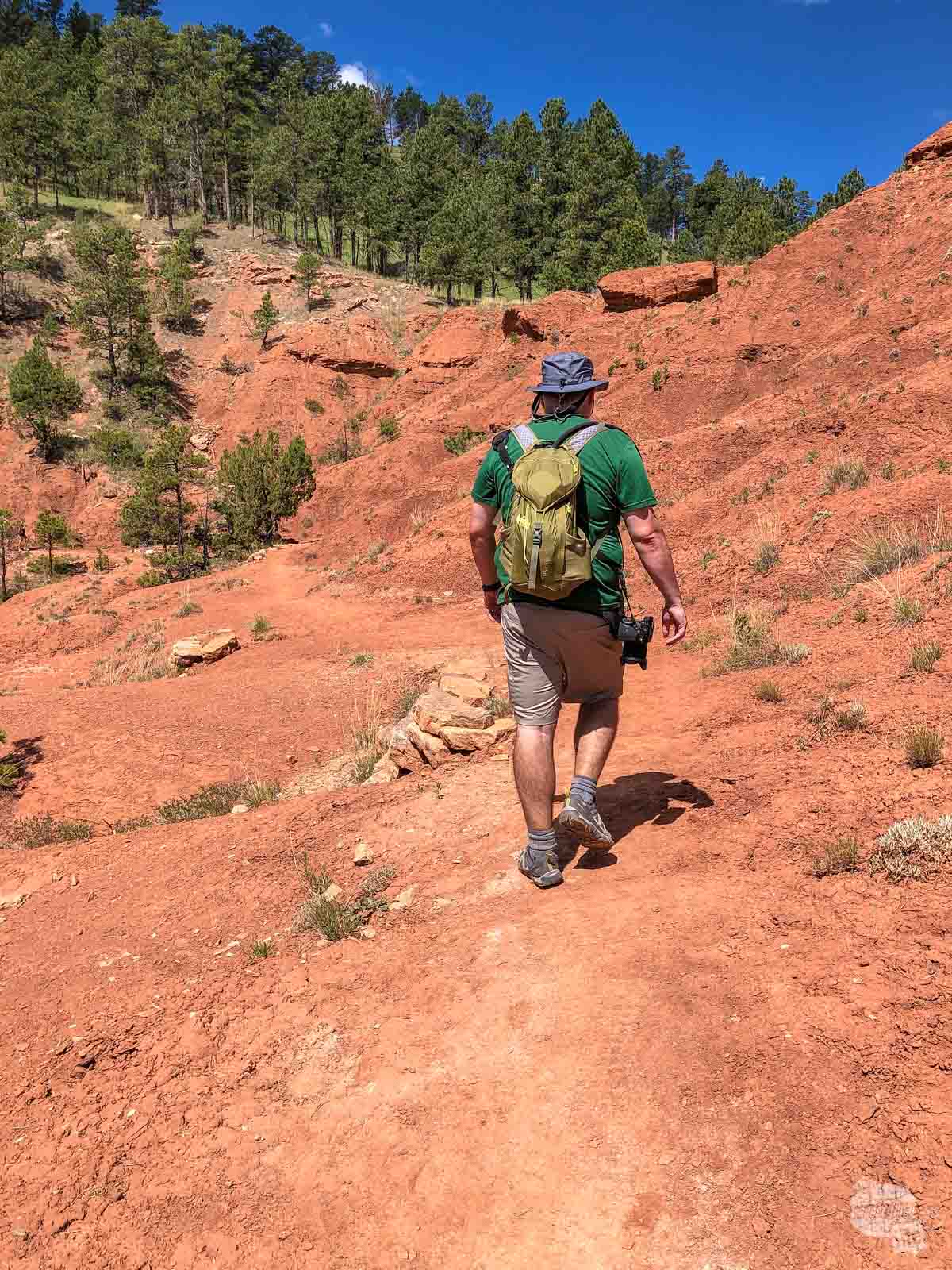 Grant Sinclair hiking the Red Beds Trail, with large amounts of red dirt surrounding him.